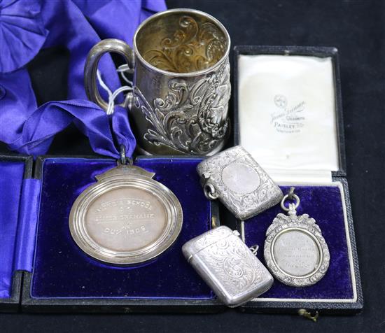 A late Victorian embossed silver christening mug, two silver vestas and two silver medallions.